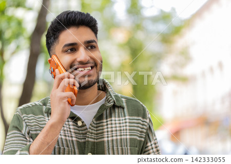 Indian man listening on smartphone walking in city street smiling while nodding during pleasant call Indian man listening on smartphone walking in city street smiling while nodding during pleasant call 142333055