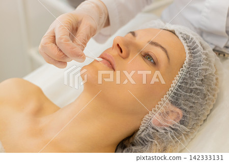 Cosmetologist applies moisturizing lip gloss on Caucasian woman for plumping beauty care in clinic 142333131