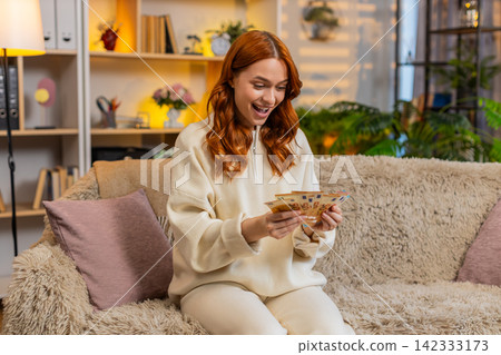 Young woman on home sofa counting cash and smiling while dreaming of shopping vacation and success Young woman on home sofa counting cash and smiling while dreaming of shopping vacation and success 142333173