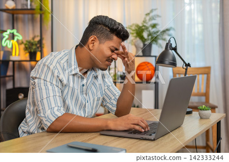 Indian man rubs eyes after long work on laptop feels pain eye strain needs pause and relief at desk 142333244
