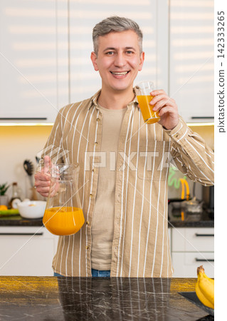 Middle-aged man drinking orange juice in kitchen at home smiling during healthy breakfast lifestyle Middle-aged man drinking orange juice in kitchen at home smiling during healthy breakfast lifestyle 142333265
