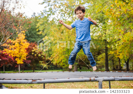 Young Boy Jumping on Trampoline Among Autumn Trees Young Boy Jumping on Trampoline Among Autumn Trees 142333323
