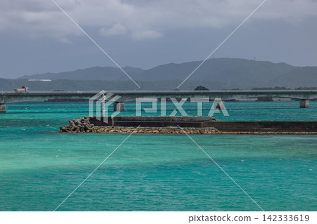 從日本沖繩縣眺望古里橋和矢賀地島,可以看到蔚藍的大海和海岸線。 從日本沖繩縣眺望古里橋和矢賀地島,可以看到蔚藍的大海和海岸線。 142333619
