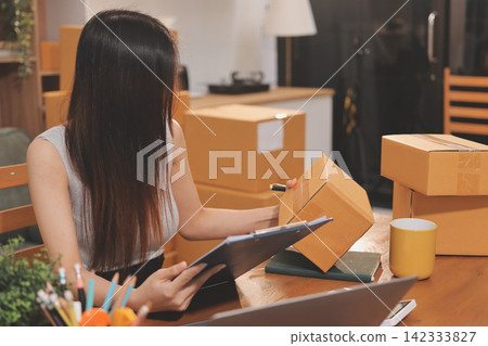 Startup SME small business entrepreneur of freelance Asian woman wearing apron using laptop and box to receive and review orders online to prepare to pack sell to customers, online sme business ideas. Startup SME small business entrepreneur of freelance Asian woman wearing apron using laptop and box to receive and review orders online to prepare to pack sell to customers, online sme business ideas. 142333827