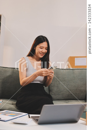 Startup SME small business entrepreneur of freelance Asian woman wearing apron using laptop and box to receive and review orders online to prepare to pack sell to customers, online sme business ideas. Startup SME small business entrepreneur of freelance Asian woman wearing apron using laptop and box to receive and review orders online to prepare to pack sell to customers, online sme business ideas. 142333834