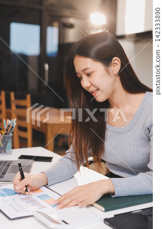 Young asian businesswoman is smiling and working on a laptop while sitting at her desk in a modern office 142333890