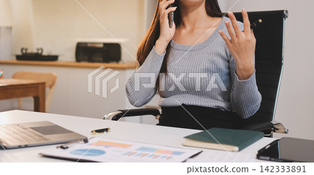 Young asian businesswoman is smiling and working on a laptop while sitting at her desk in a modern office Young asian businesswoman is smiling and working on a laptop while sitting at her desk in a modern office 142333891