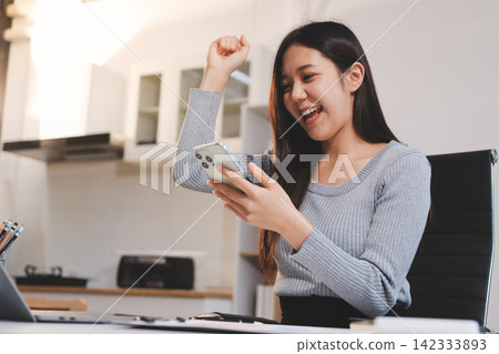 Young asian businesswoman is smiling and working on a laptop while sitting at her desk in a modern office Young asian businesswoman is smiling and working on a laptop while sitting at her desk in a modern office 142333893