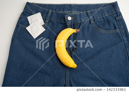 Banana with measuring tape and condom on jean trousers, penis health. Banana with measuring tape and condom on jean trousers, penis health. 142333961