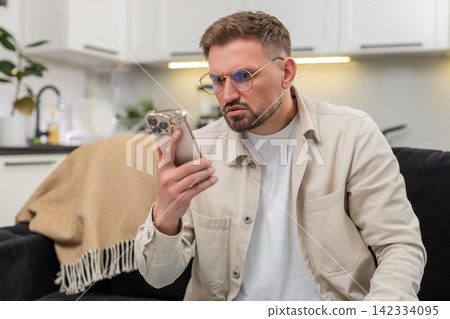 Young man with glasses checks smartphone reads tiny text surprised by news vision aid improves focus Young man with glasses checks smartphone reads tiny text surprised by news vision aid improves focus 142334095