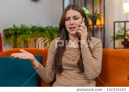 Young woman argues on smartphone frowns sharp hand moves raises voice and speaks fast in tense call Young woman argues on smartphone frowns sharp hand moves raises voice and speaks fast in tense call 142334183