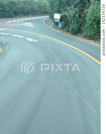 A winding road with a series of corners and lush green street trees. A winding road with a series of corners and lush green street trees. 142334729
