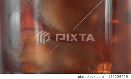 Cold drink in a glass with ice cubes and condensation, macro view showing refreshing brown liquid Cold drink in a glass with ice cubes and condensation, macro view showing refreshing brown liquid 142334759