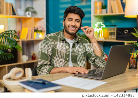 Indian man on home table call center operator with headset working with client on laptop video call 142334985