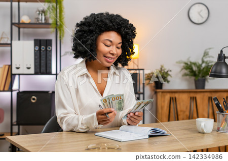 African American businesswoman counts dollar cash notes family budget writes expenses on notebook African American businesswoman counts dollar cash notes family budget writes expenses on notebook 142334986