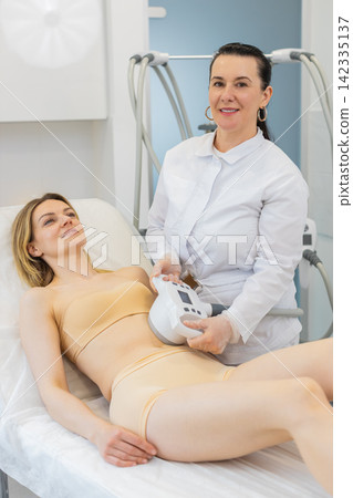 Middle-aged woman receives LPG vacuum massage on abdomen for body contouring in beauty clinic salon Middle-aged woman receives LPG vacuum massage on abdomen for body contouring in beauty clinic salon 142335137