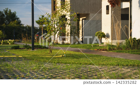 Lawn sprinkler watering green grass in a modern suburban backyard garden, providing automatic irrigation for plants Lawn sprinkler watering green grass in a modern suburban backyard garden, providing automatic irrigation for plants 142335282