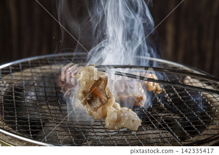 畫面中,人們正在用炭火烤架烤牛肉和內臟,筷子夾著的肉冒著熱氣。 畫面中,人們正在用炭火烤架烤牛肉和內臟,筷子夾著的肉冒著熱氣。 142335417