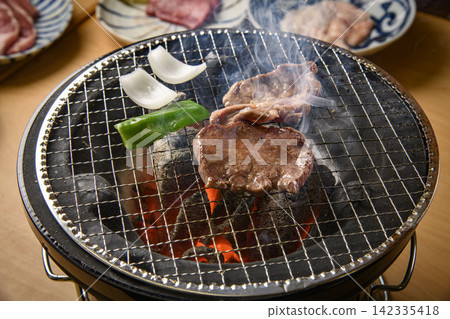 炭火烤架上烤牛肉，烹調過程中火焰升騰，還有烤白洋蔥。 142335418