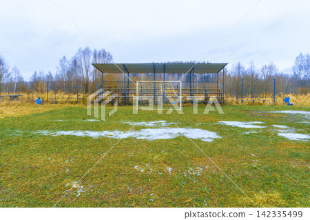 Small outdoor soccer goal with metal bleachers on muddy grass field in late winter Small outdoor soccer goal with metal bleachers on muddy grass field in late winter 142335499