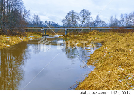 Low concrete bridge over calm river in late winter rural landscape with golden reeds 142335512