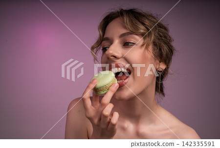 Young woman enjoying sweet green macaroon, expressing joy and indulgence on pink background Young woman enjoying sweet green macaroon, expressing joy and indulgence on pink background 142335591