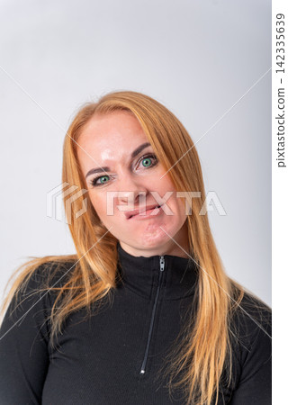 Young woman posing with a displeased facial expression, scrunching her nose and pursing her lips, communicating disapproval or distaste on a light background Young woman posing with a displeased facial expression, scrunching her nose and pursing her lips, communicating disapproval or distaste on a light background 142335639