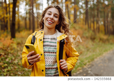 Hiking in autumn forest. Smiling tourist in bright coat walks through autumn park in sunny weather. Hiking in autumn forest. Smiling tourist in bright coat walks through autumn park in sunny weather. 142335668