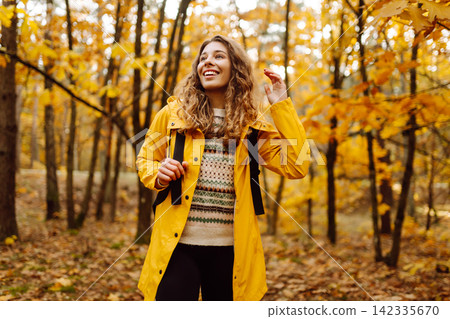 Hiking in autumn forest. Smiling tourist in bright coat walks through autumn park in sunny weather. Hiking in autumn forest. Smiling tourist in bright coat walks through autumn park in sunny weather. 142335670