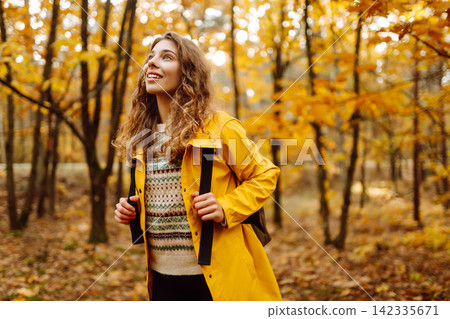 Hiking in autumn forest. Smiling tourist in bright coat walks through autumn park in sunny weather. Hiking in autumn forest. Smiling tourist in bright coat walks through autumn park in sunny weather. 142335671