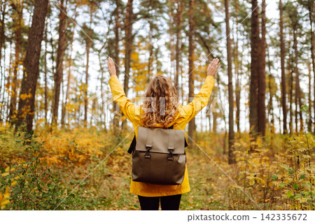 Back view. Curly woman with backpack in autumn forest enjoying nature. Concept of relaxation, nature Back view. Curly woman with backpack in autumn forest enjoying nature. Concept of relaxation, nature 142335672