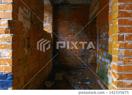 Narrow unfinished brick corridor inside abandoned building with scattered debris and painted mortar Narrow unfinished brick corridor inside abandoned building with scattered debris and painted mortar 142335675