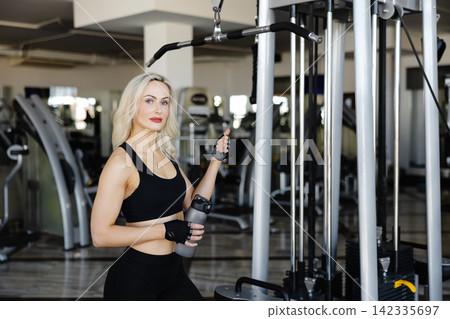 Determined sportswoman holding water bottle and training in gym Determined sportswoman holding water bottle and training in gym 142335697