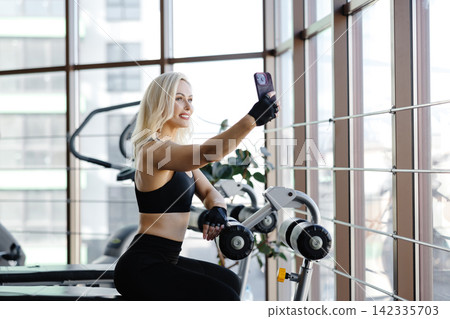 Athletic woman resting on bench after exercising with dumbbells in gym Athletic woman resting on bench after exercising with dumbbells in gym 142335703