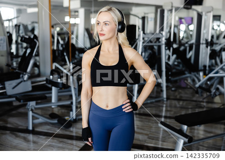 Athletic woman wearing headphones posing in the gym Athletic woman wearing headphones posing in the gym 142335709