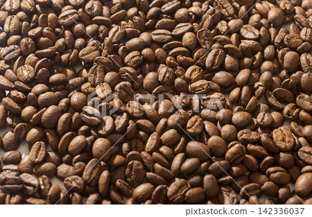 A wide spread of roasted coffee beans fills a horizontal frame from edge to edge. The even layer of dark brown beans creates a consistent textured background. Concept of coffee A wide spread of roasted coffee beans fills a horizontal frame from edge to edge. The even layer of dark brown beans creates a consistent textured background. Concept of coffee 142336037