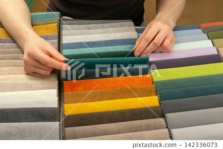 Fingers lifting a single fabric swatch from the row. Hand selecting a specific textile color among Fingers lifting a single fabric swatch from the row. Hand selecting a specific textile color among 142336073
