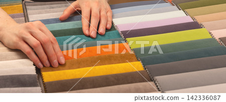 Hands touching rows of textile swatches on table. Someone examining fabric colors for a design 142336087