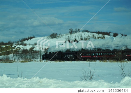 SL 冬季沼澤地列車:一輛動力強勁的蒸汽機車行駛在北海道東部白雪皚皚的景色中。 SL 冬季沼澤地列車:一輛動力強勁的蒸汽機車行駛在北海道東部白雪皚皚的景色中。 142336484