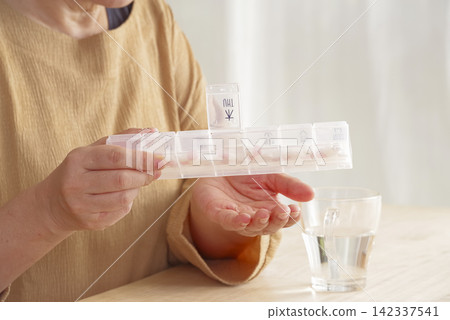 A woman using a pill case to manage her medication. A woman using a pill case to manage her medication. 142337541