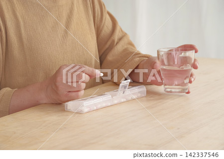 A woman using a pill case to manage her medication. A woman using a pill case to manage her medication. 142337546