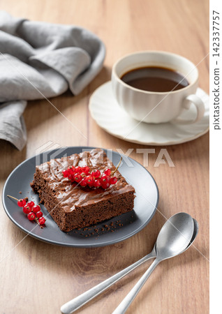 Pieces of chocolate brownie with redcurrant on a plate and a cup of espresso coffee Pieces of chocolate brownie with redcurrant on a plate and a cup of espresso coffee 142337757