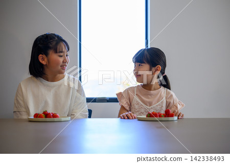 Sisters smiling at a table with strawberries in front of them. Sisters smiling at a table with strawberries in front of them. 142338493