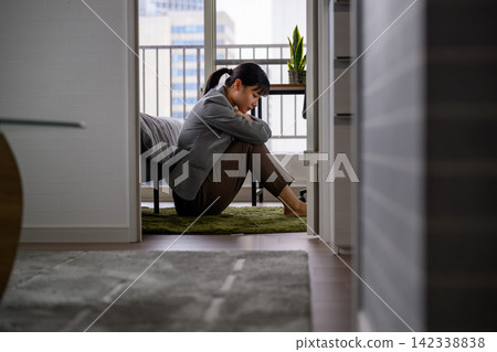 A woman with her head bowed in her room; worries, stress, loneliness. A woman with her head bowed in her room; worries, stress, loneliness. 142338838