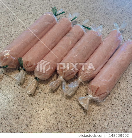 High angle view of raw homemade chicken sausages wrapped in plastic film on kitchen countertop table surface square stock photo High angle view of raw homemade chicken sausages wrapped in plastic film on kitchen countertop table surface square stock photo 142339902