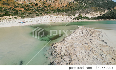 Aerial perspective of Balos Bay featuring clear turquoise waters with distinct algae patches, a sandy beach, and rocky hills in the background, highlighting the natural beauty of Crete, Greece Aerial perspective of Balos Bay featuring clear turquoise waters with distinct algae patches, a sandy beach, and rocky hills in the background, highlighting the natural beauty of Crete, Greece 142339903