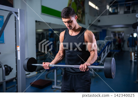 Focused bodybuilder doing a bicep curl with a straight barbell Focused bodybuilder doing a bicep curl with a straight barbell 142340025