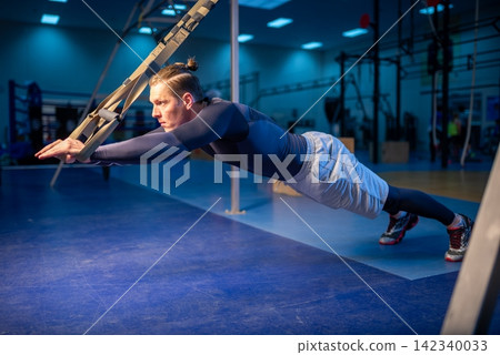 Man maintaining a straight plank position with straps Man maintaining a straight plank position with straps 142340033