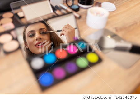 Reflection of a young woman applying shadow in a small cosmetic mirror Reflection of a young woman applying shadow in a small cosmetic mirror 142340079