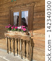 Traditional alpine wooden house wall facade with a window and a flower box filled with blooming pink geraniums in Hausham, Upper Bavaria, Germany. 142340300